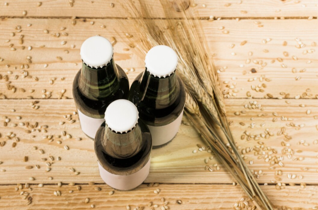 three green bottles with white bottle caps, ears of wheat on wooden table