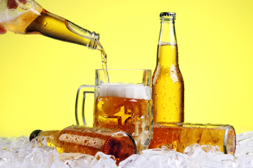 Beer is pouring into glass from a bottle, three bottles of beer on the ice cubes on a yellow background
