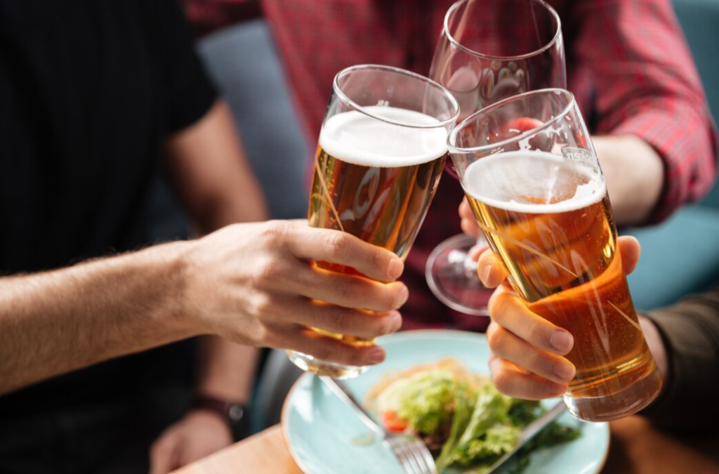 three persons clinking glasses of beer, the blue plate on the table with salad on it 