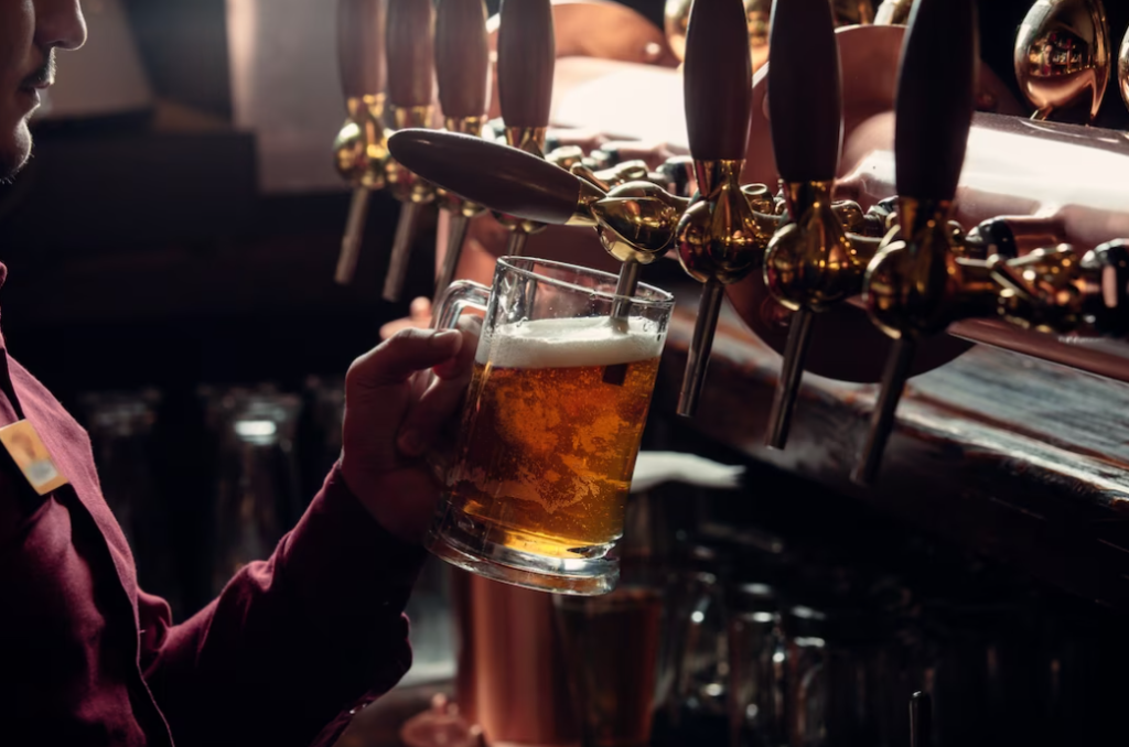 Bartender in red shirt fills beer mug from beer tap in the semi-darkness 