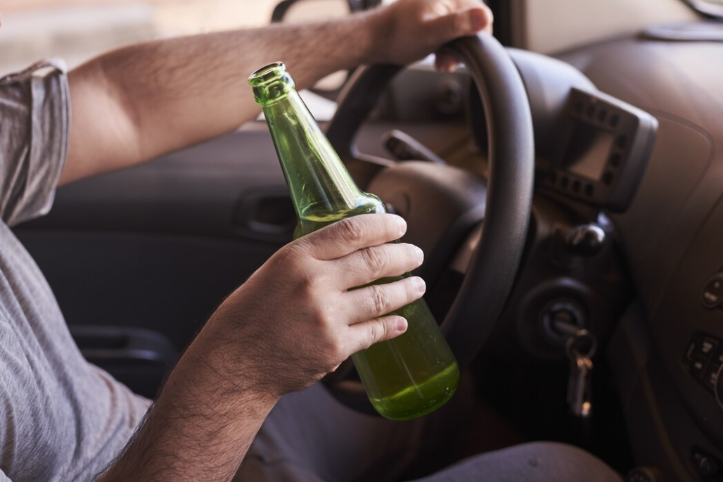 man in gray t-shirt hold a car wheel with one hand, and bottle of beer in another