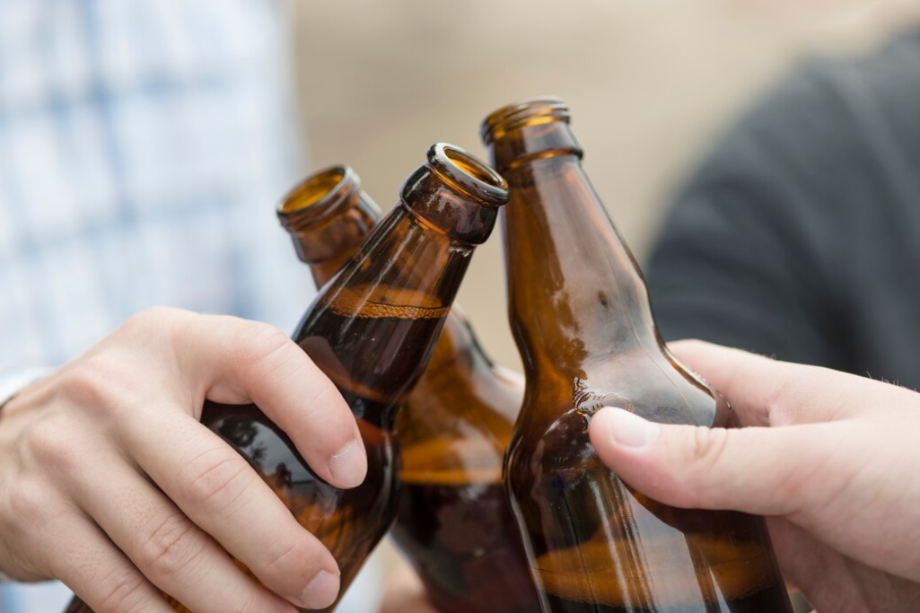 a close up view of three hands clinking with brown beer bottles outside