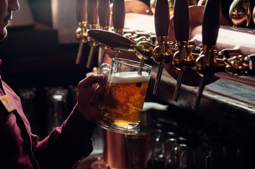Bartender in red shirt fills beer mug from beer tap in the semi-darkness
